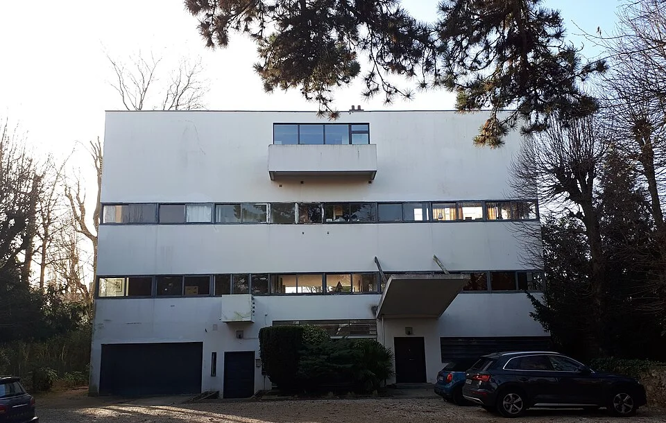 weißes Gebäude in Form eines Quaders mit zwei schmalen Fensterreihen und einem Balkon