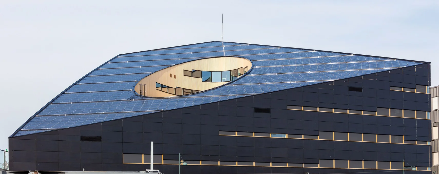 Office block with a dark façade and a sloping roof fitted with solar panels