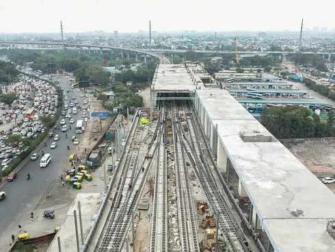 Bird's-eye view of a railway line and station under construction next to a road with a city in the background