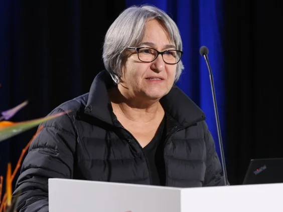 Foto einer Frau mit Brille und grauen Haaren auf einem Podium