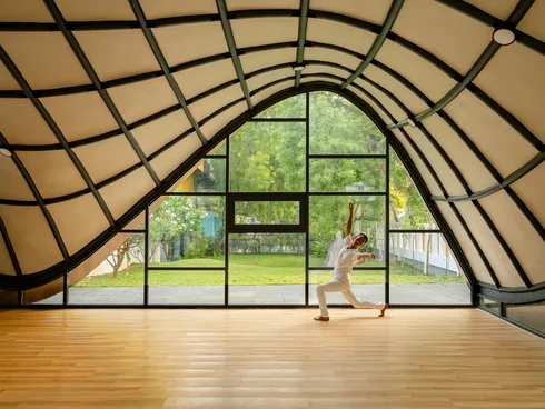 Tänzer auf Parkettboden vor Glasfront und unter geschwungenem Dach