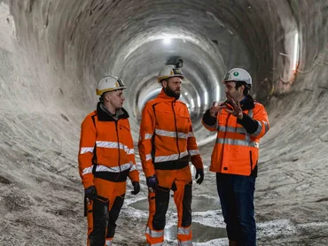 Drei Bauarbeiter unterhalten sich in einem unfertigen Tunnel