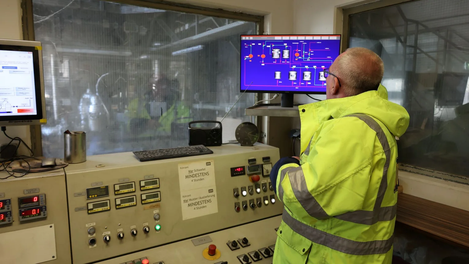 Mann in gelber PORR Jacke steht vor einem Kontrollpult und schaut auf einen Bildschirm