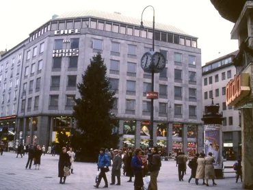 Post-war building in the background, in front of it a square with people