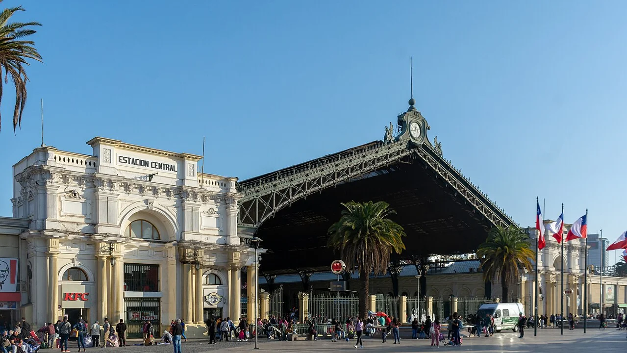 Bahnhofsvorplatz mit Bahnhofshalle, spitzem Dach und Uhr