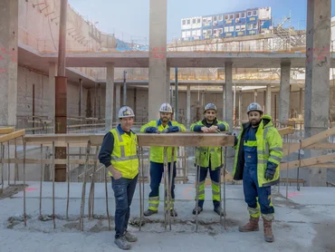 vier Bauarbeiter in der Baugrube. Containerburg im Hintergrund