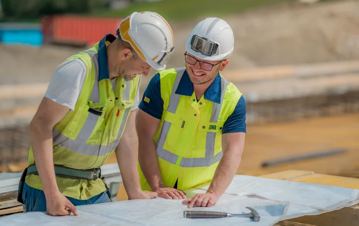Two workers on a building site with a construction plan