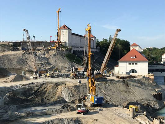 A large construction site below a historic building with several cranes and construction equipment working on site preparation.