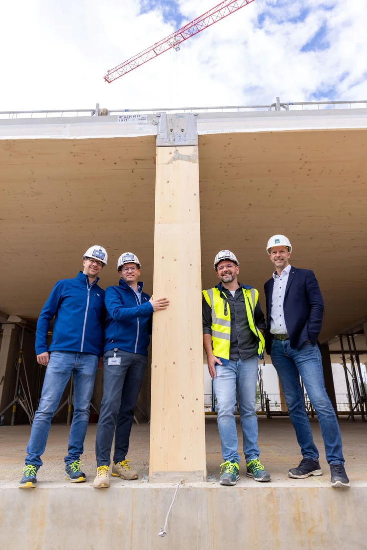 Four people wearing hard hats are standing around a wooden pillar